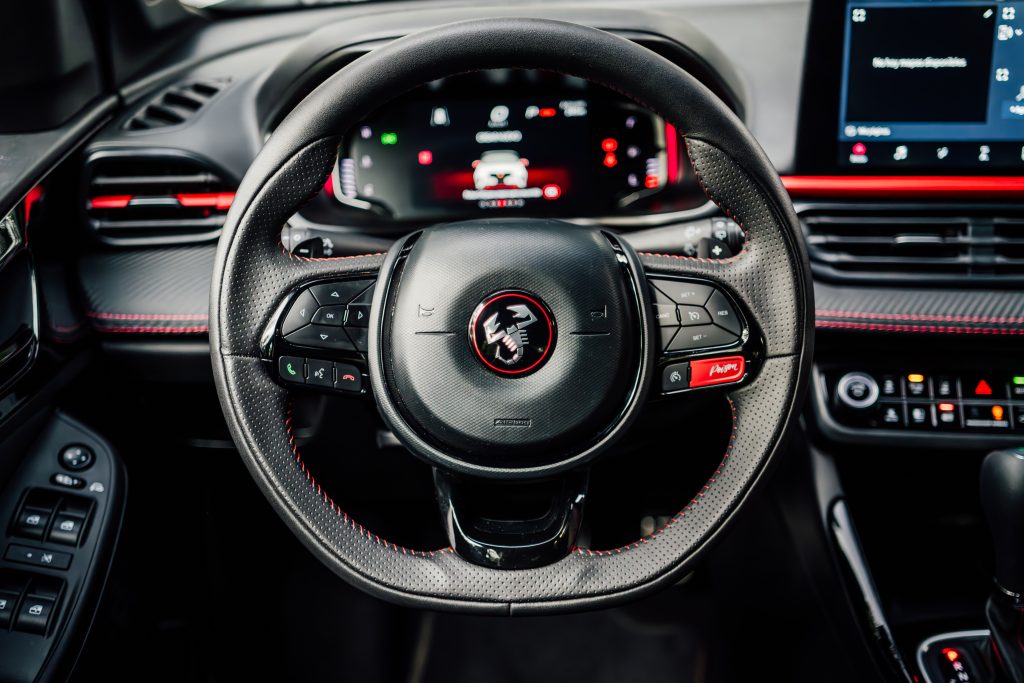 Diseño interior deportivo y elegante. Volante de cuero negro con costuras rojas y logo de Abarth, que añade un toque de exclusividad al habitáculo.